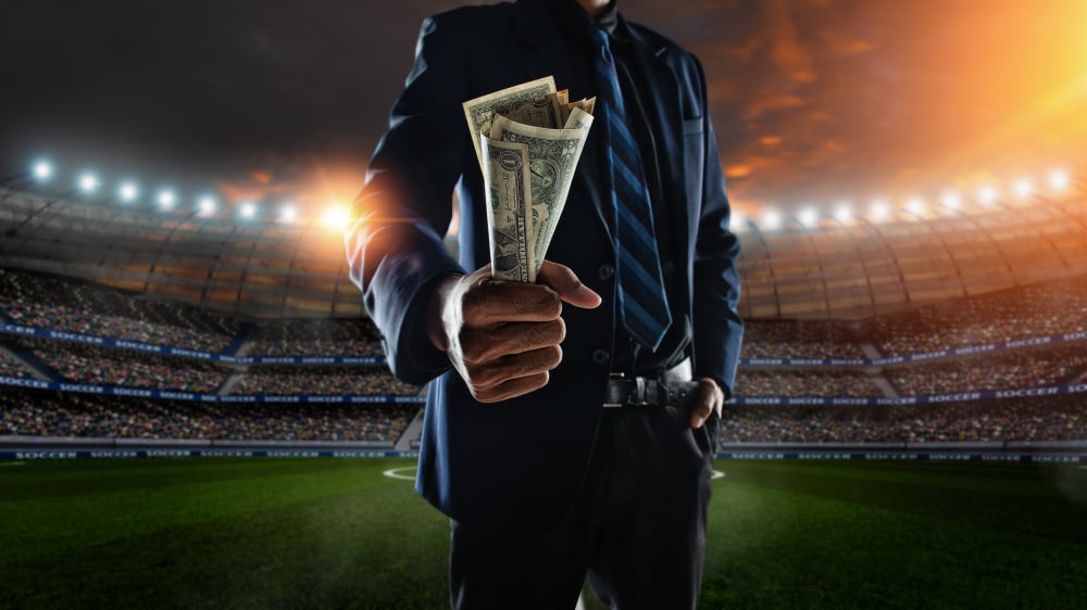 Businessman holding a wad of cash in a sports stadium