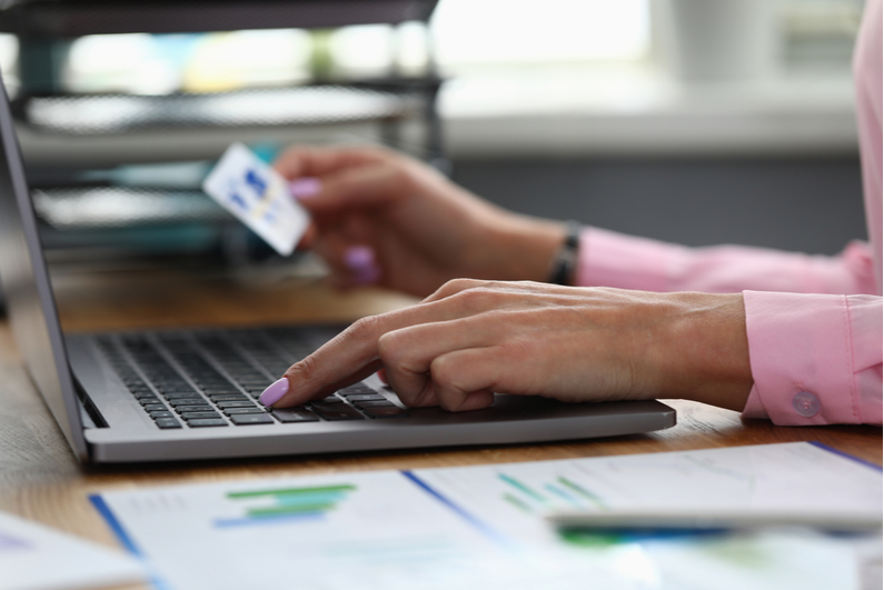 Hand holding a card while making an online deposit on a laptop